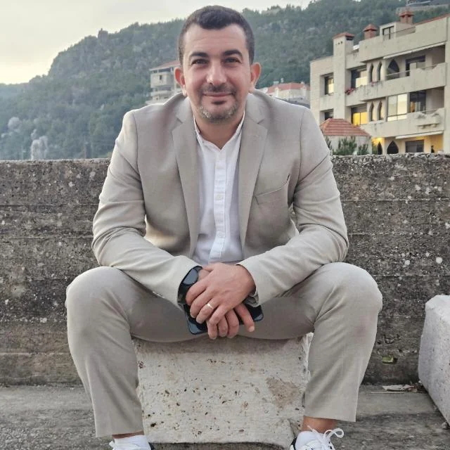 Charbel Assaf in a beige suit with the mountains of Lebanon behind him